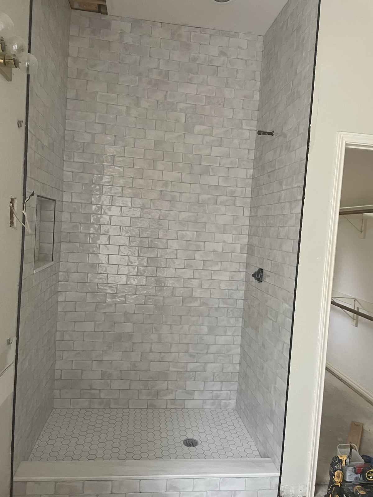 Finished walk-in shower with subway tile walls, hex tile floor, and recessed niche