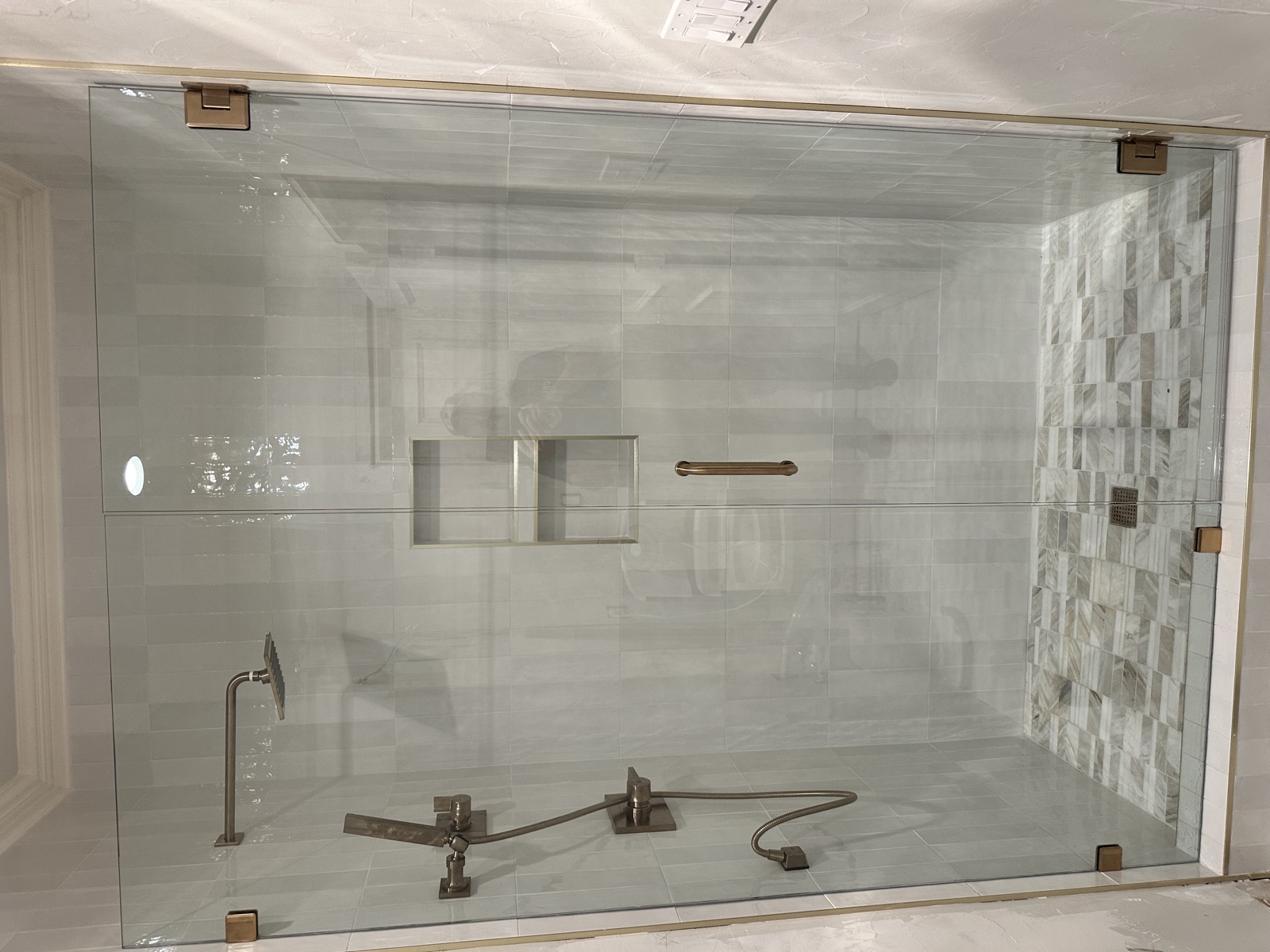 Frameless glass shower with marble mosaic accent wall and tiled niche